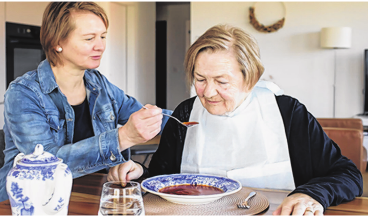 Eine Angehörige unterstützt eine ältere Frau beim Essen – ein Beispiel für die wertvolle Pflegearbeit zu Hause, die heute auch finanziell entschädigt werden kann.